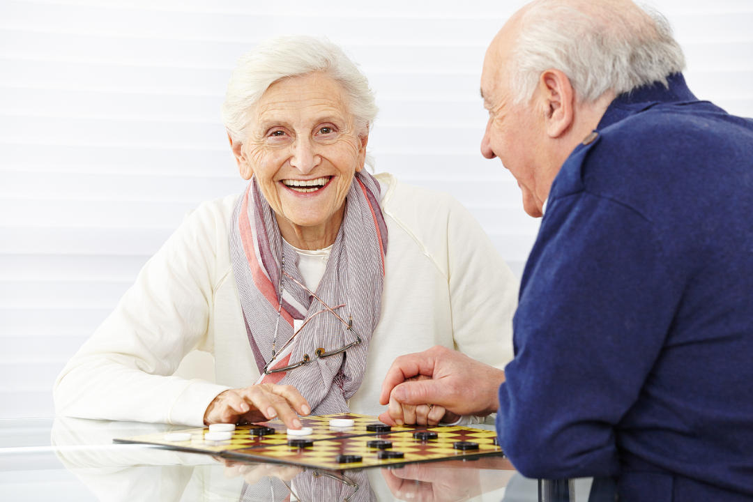Happy senior couple playing checkers in a retirement home